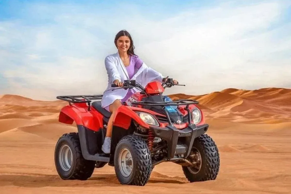 Rider kicking up dust on a single seater quad bike across open desert sand in Dubai